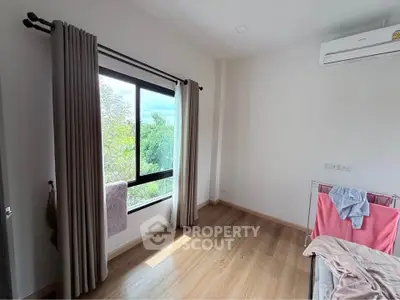 Bright bedroom with large window and air conditioning, offering a serene view of greenery.