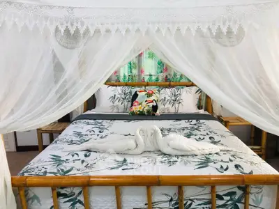 Charming bedroom with bamboo bed and elegant canopy, featuring tropical-themed decor and swan towel art.