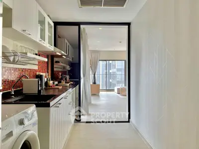 Modern kitchen with open layout and washing machine, leading to bright living area with large windows.