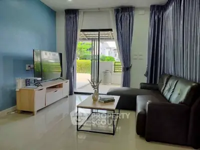 Modern living room with sleek black sofa and large TV, opening to a lush garden view.