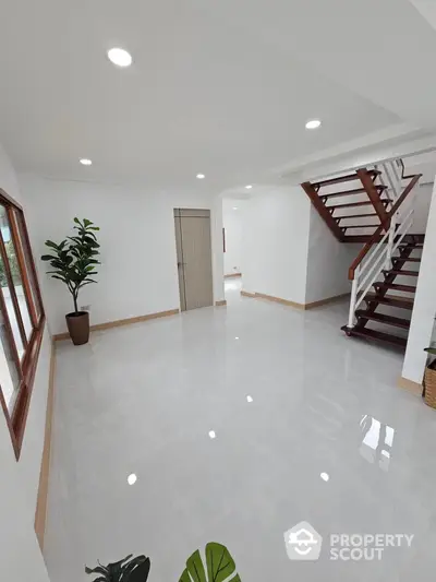 Spacious and bright living area with glossy tiled floors, modern staircase, and ample natural light, perfect for family gatherings and stylish living.