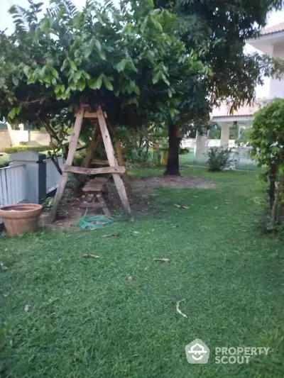 Charming garden with lush greenery and a rustic wooden swing, perfect for relaxation and outdoor enjoyment.