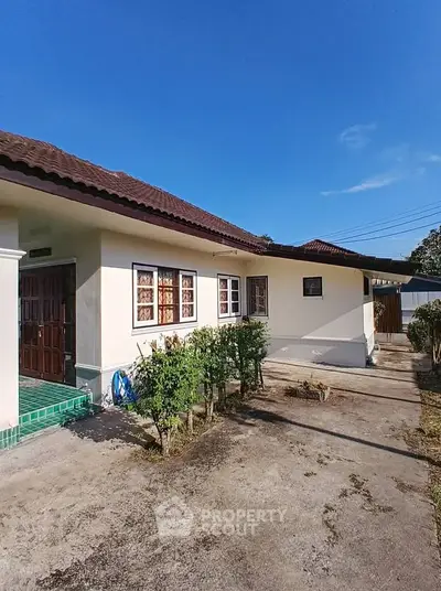 Charming single-story home with lush garden and spacious driveway under clear blue skies.