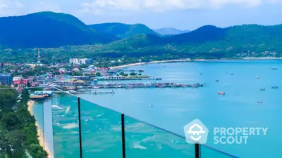 Stunning coastal view from a high-rise balcony overlooking serene blue waters and lush green hills.