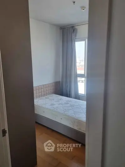 Cozy bedroom with natural light and wooden flooring, featuring a single bed and modern curtains.