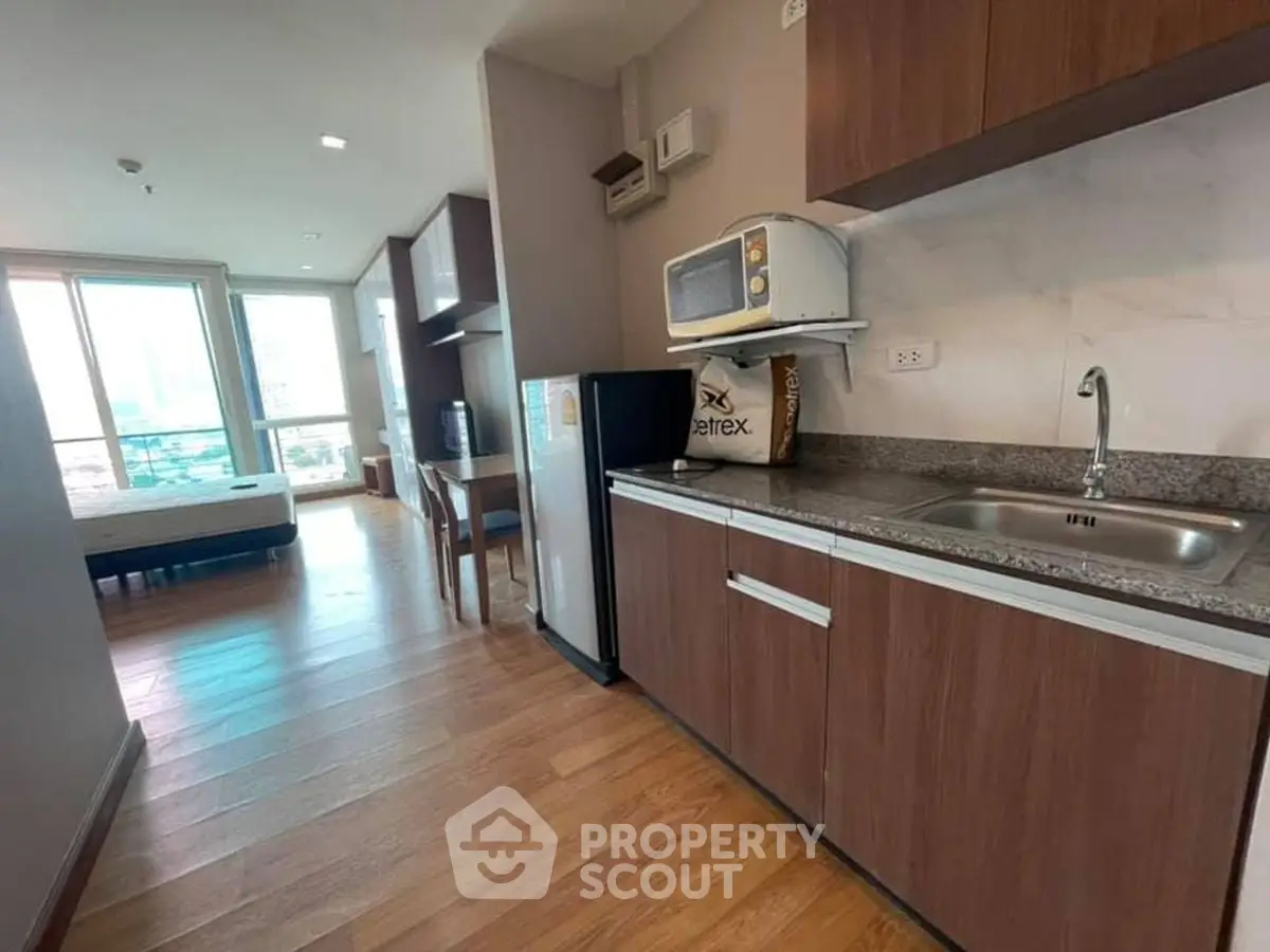 Modern studio apartment with kitchenette and city view, featuring wooden flooring and ample natural light.