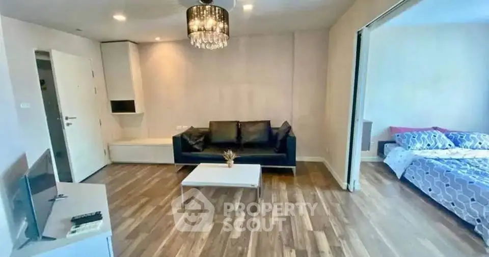 Modern open-plan living room with elegant chandelier and cozy bedroom view.