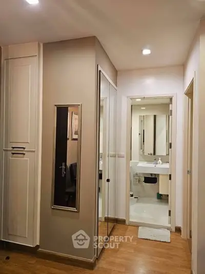 Modern apartment hallway with mirrored closet and view into sleek bathroom.