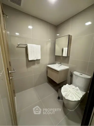 Modern bathroom with sleek fixtures and neutral tiles, featuring a wall-mounted sink and a towel rack.