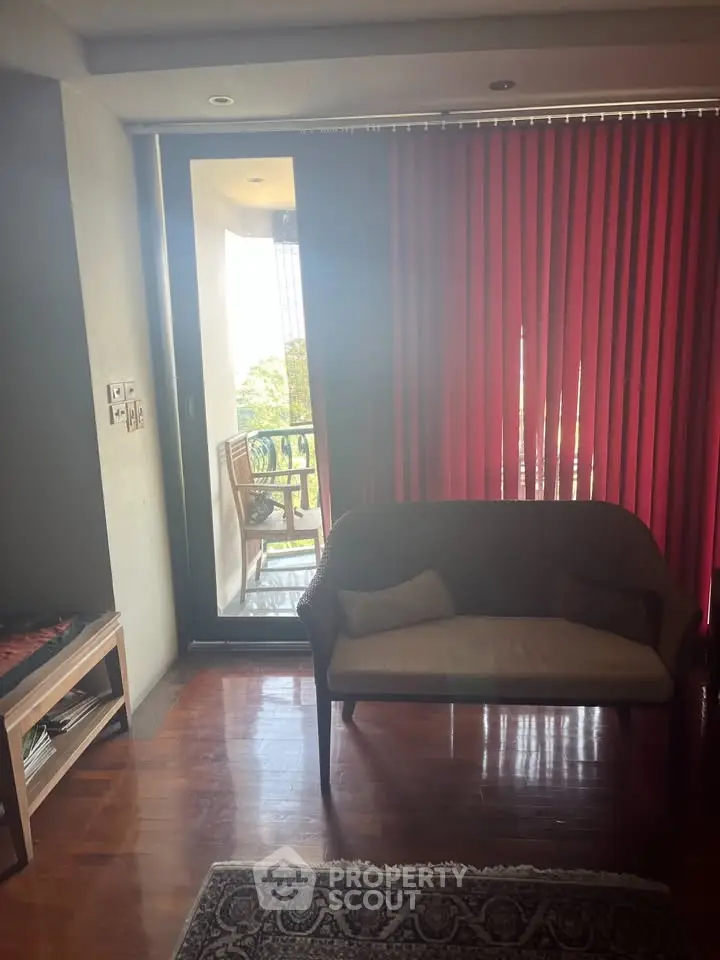 Cozy living room with red blinds and balcony view, featuring a stylish sofa and wooden flooring.