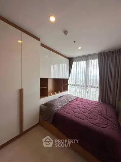 Modern bedroom with large window and built-in wardrobe in a high-rise apartment.