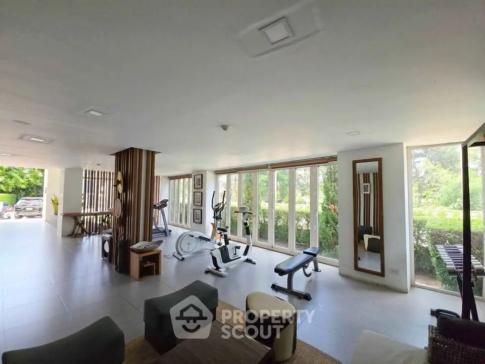 Spacious gym with modern equipment and large windows offering garden views.
