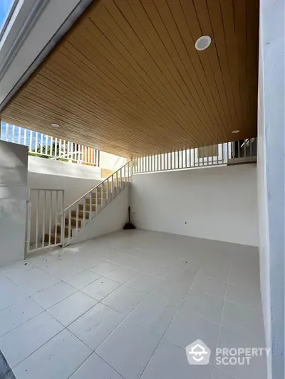 Spacious white-tiled outdoor area with wooden ceiling and staircase, perfect for versatile use.