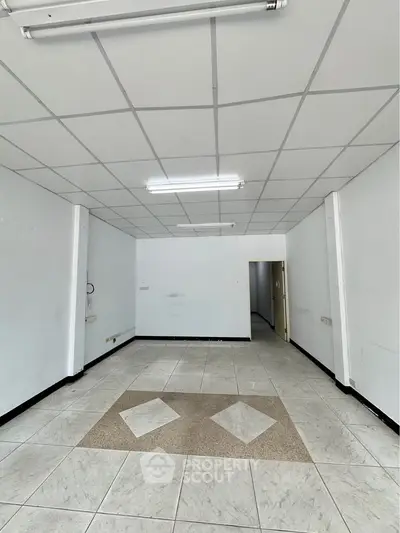 Spacious empty room with tiled flooring and ceiling lights, ideal for office or retail space.