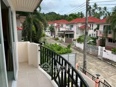 Charming balcony view overlooking a serene residential neighborhood with lush greenery and red-roofed houses.