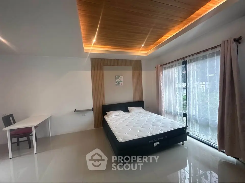 Spacious bedroom with modern ceiling design and large window for natural light.