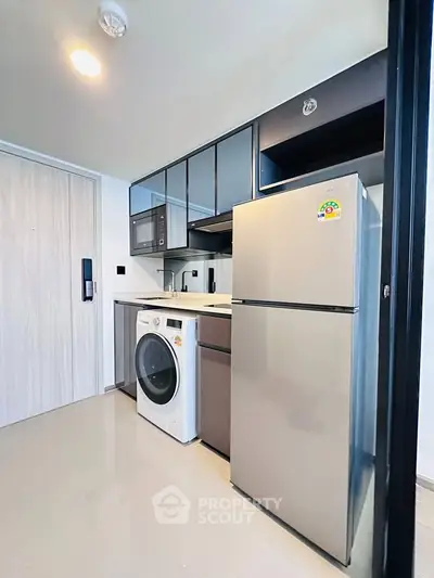 Modern kitchen with sleek appliances including fridge and washing machine in compact layout.