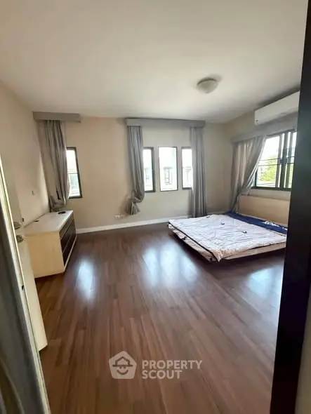 Spacious bedroom with wooden flooring and large windows for natural light.