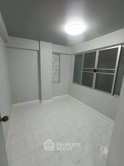 Spacious empty room with modern tiled flooring and large windows, perfect for customization.