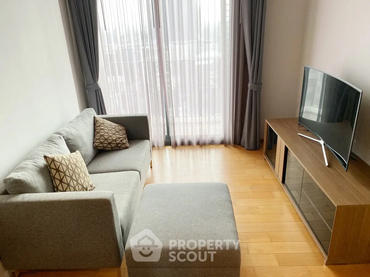 Modern living room with stylish sofa and TV, featuring floor-to-ceiling windows and elegant curtains.