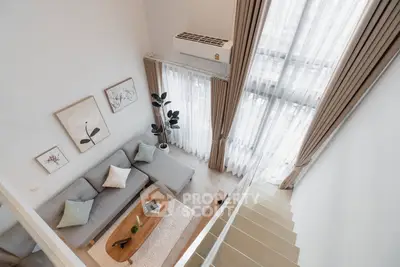 Modern living room with high ceiling and large windows, featuring stylish decor and cozy seating area.