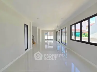 Spacious open-plan living room with large windows and glossy tiled floors in modern home.