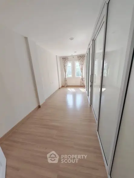 Bright and spacious room with wooden flooring and large windows in modern apartment.