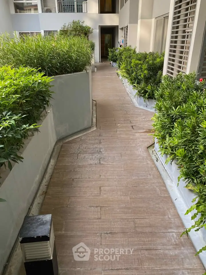 Modern apartment building entrance with lush greenery and wooden pathway.