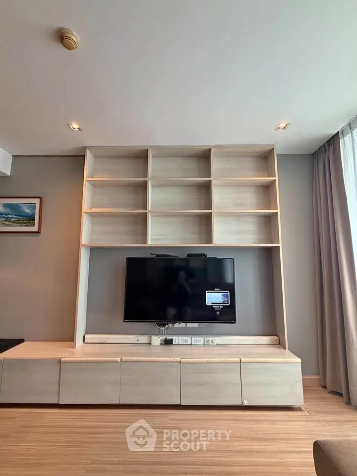 Modern living room with built-in TV unit and shelving, featuring sleek design and natural light.
