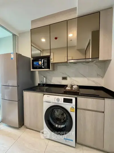 Modern kitchen with sleek cabinetry, washing machine, and stainless steel fridge in compact layout.