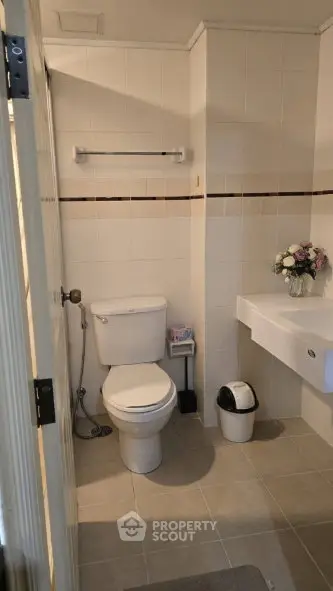 Modern bathroom with white tiles, toilet, and sink, featuring elegant floral decor.