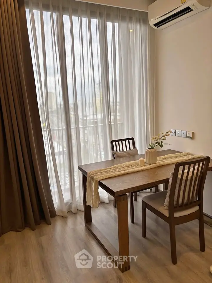 Cozy dining area with wooden table and chairs, large window with sheer curtains, and air conditioning.