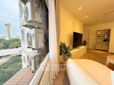 Modern living room with city view and air conditioning units outside the window.