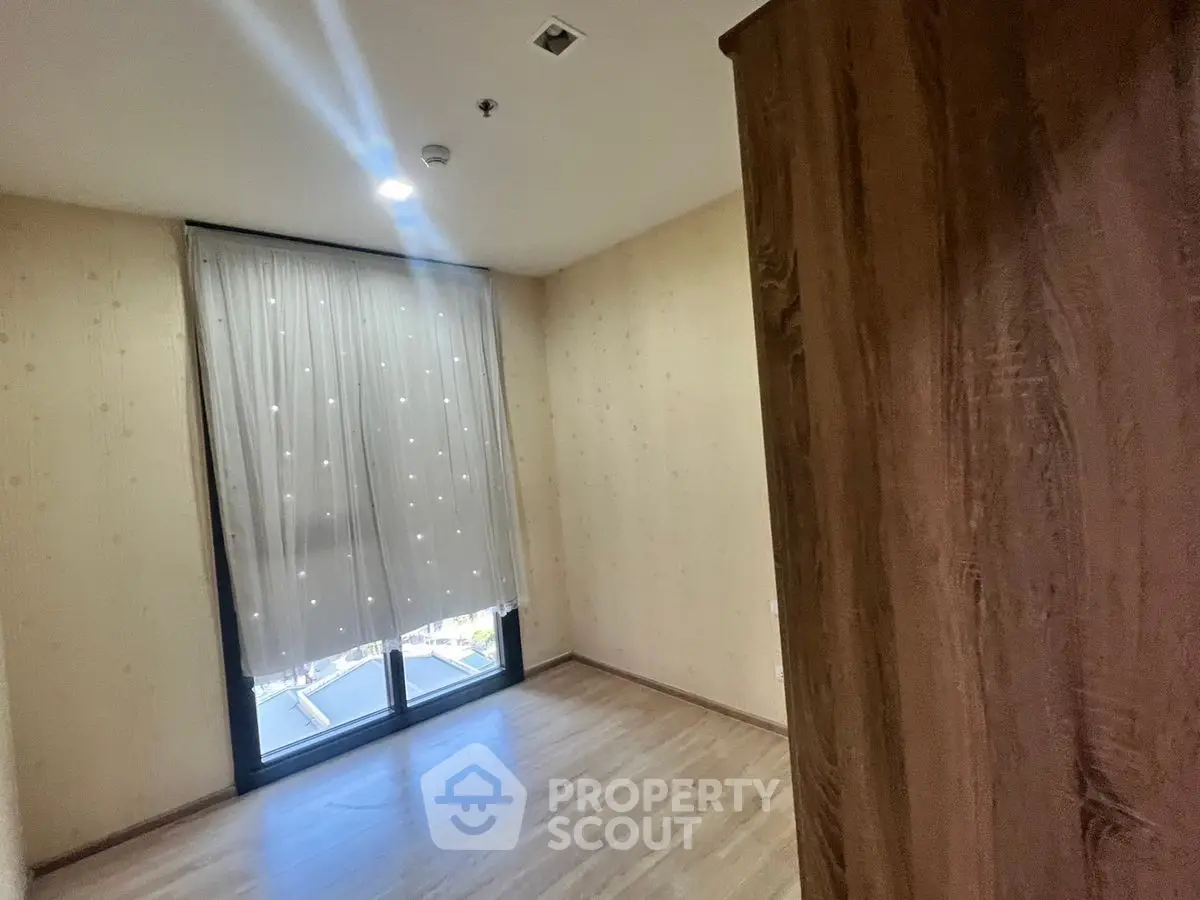 Spacious empty room with wooden flooring and large window, perfect for customization.