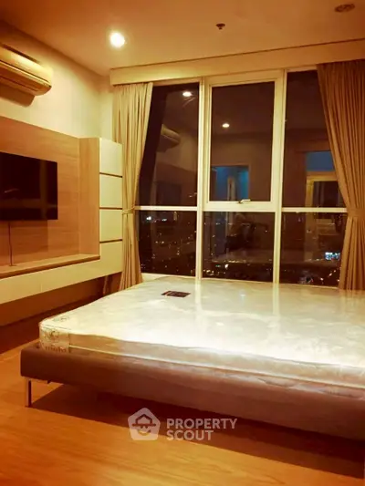Modern bedroom with large window and city view, featuring a mounted TV and air conditioning.
