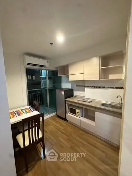 Modern kitchen with wooden flooring, compact dining area, and balcony access in a cozy apartment.