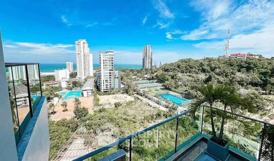 Stunning high-rise balcony view overlooking cityscape and lush greenery with ocean in the distance.