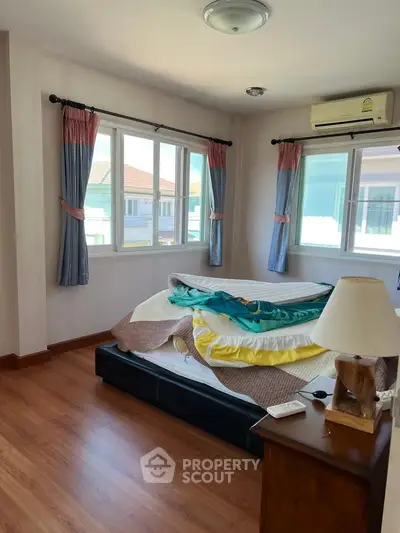 Spacious bedroom with large windows and wooden flooring, featuring a cozy bed and air conditioning.
