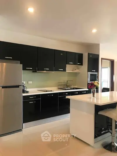 Modern kitchen with sleek black cabinets and stainless steel appliances, featuring a stylish island and open layout.