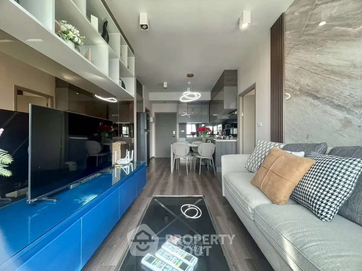Modern living room with sleek design, featuring a large TV, stylish furniture, and open kitchen layout.