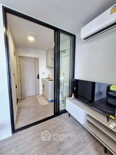 Modern compact living room with sliding glass door to kitchen, featuring sleek furniture and air conditioning.