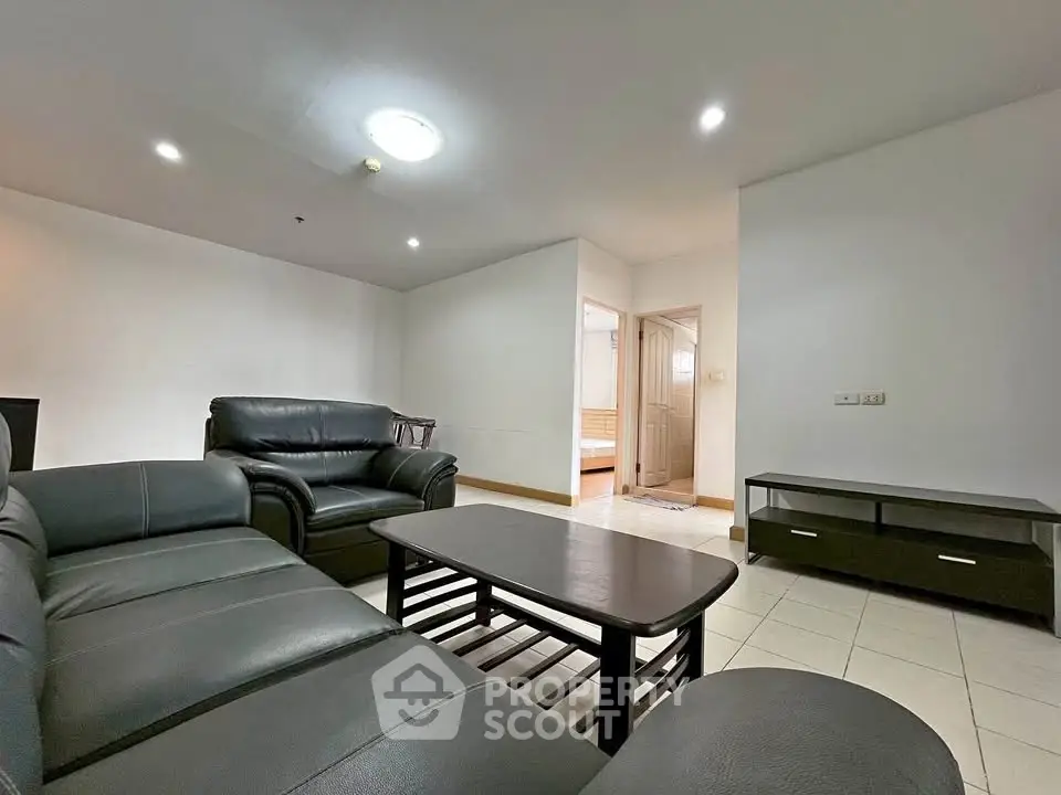 Spacious living room with modern black leather sofa and sleek coffee table in a well-lit apartment.