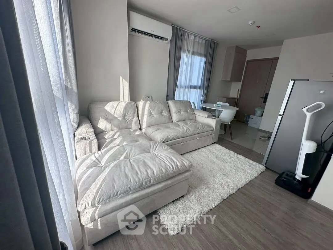 Modern living room with plush sofa, air conditioning, and sleek kitchen area in open layout apartment.