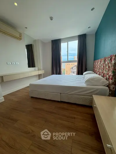 Spacious bedroom with wooden flooring and large window offering city views.