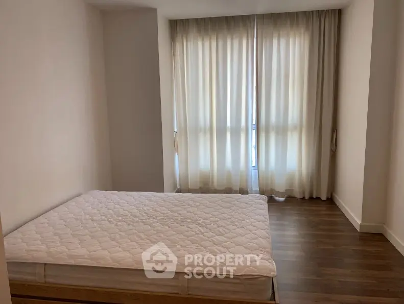 Spacious bedroom with large window and elegant curtains, featuring a comfortable bed and wooden flooring.