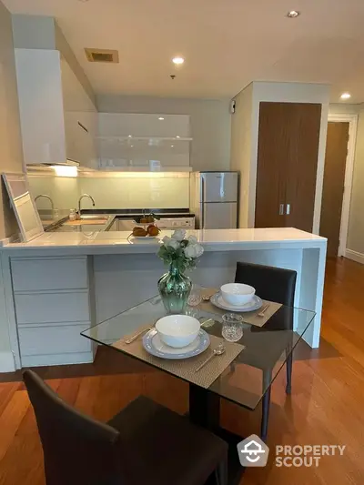 Modern kitchen with sleek design and dining area featuring glass table and stylish chairs.