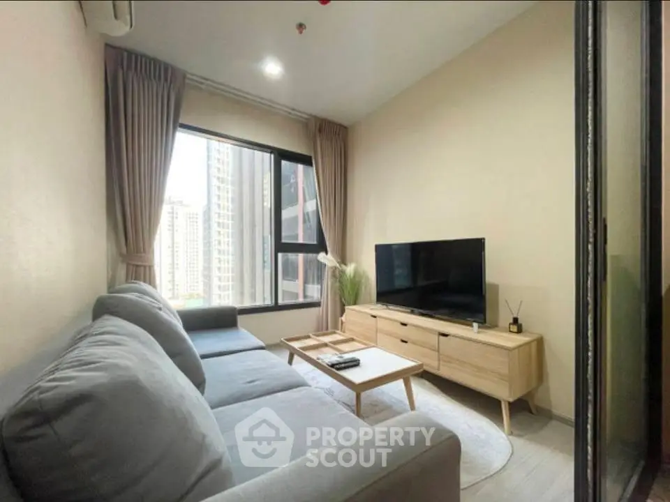 Modern living room with large window and city view, featuring a cozy sofa and sleek TV setup.