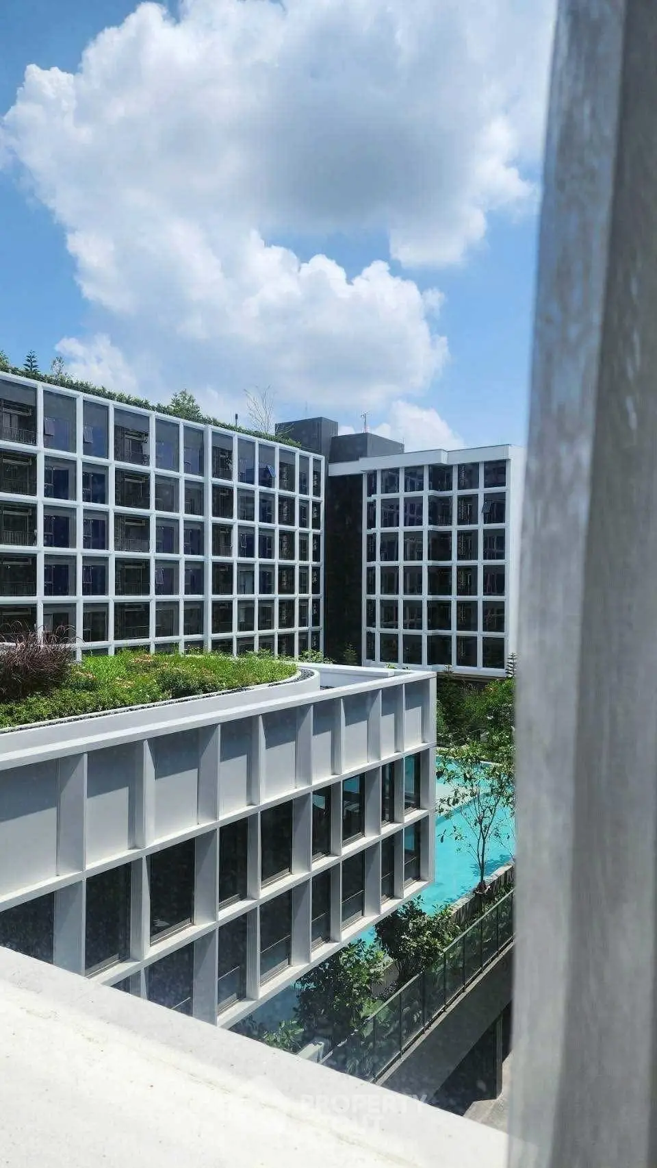 Modern apartment complex with pool and lush greenery under a bright blue sky.