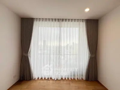Bright room with large window and elegant curtains, offering a serene city view.