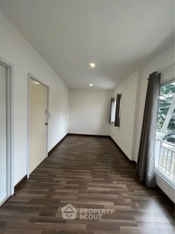 Spacious and well-lit empty room with elegant dark wooden flooring, crisp white walls, and large windows draped with stylish curtains, perfect for a personalized interior design.